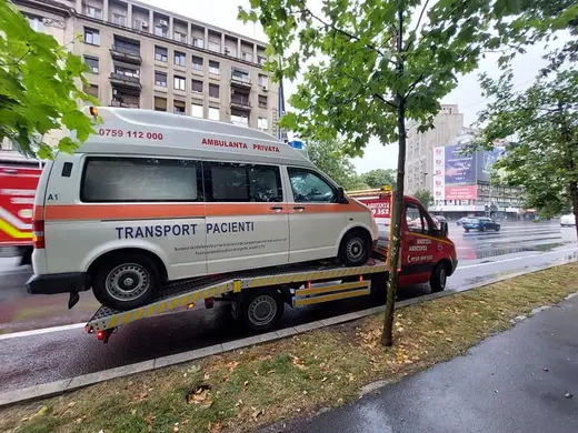 Autoutilitară de transport pacienți încărcată pe platformă, pe stradă în ploaie