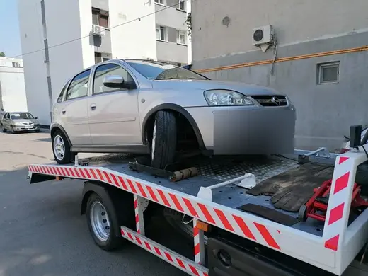 Autoturism hatchback argintiu încărcat pe platforma hidraulică, în curte interioară de bloc