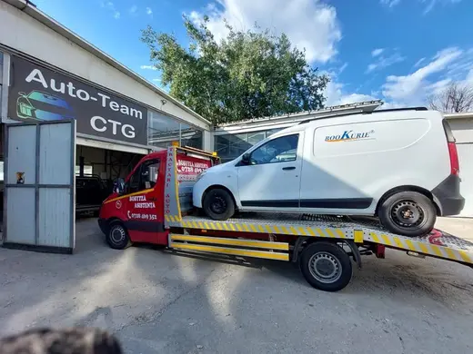 Autoutilitară albă de curierat încărcată pe platformă, lângă un service auto