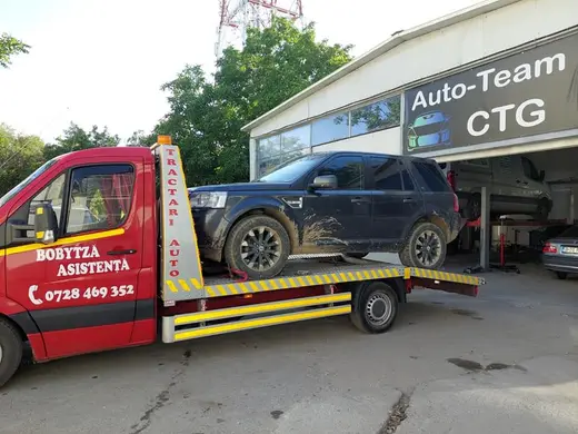 SUV negru încărcat pe platforma hidraulică, în fața unui service auto