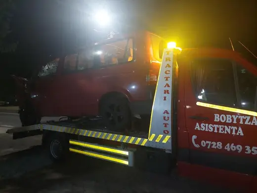 Microbuz roșu încărcat pe platformă, tractat noaptea pe marginea drumului