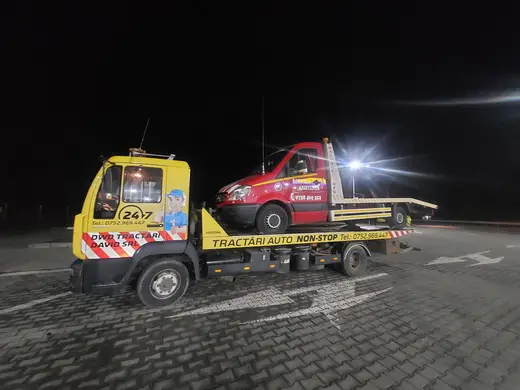 Autoutilitară roșie de tractări cu o dubă încărcată pe platformă, noaptea în parcare