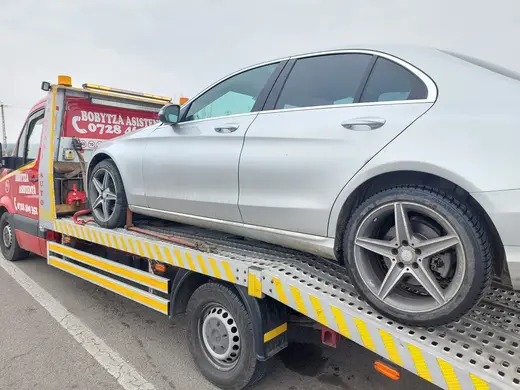 Sedan argintiu încărcat pe platforma hidraulică, remorcat pe un drum public