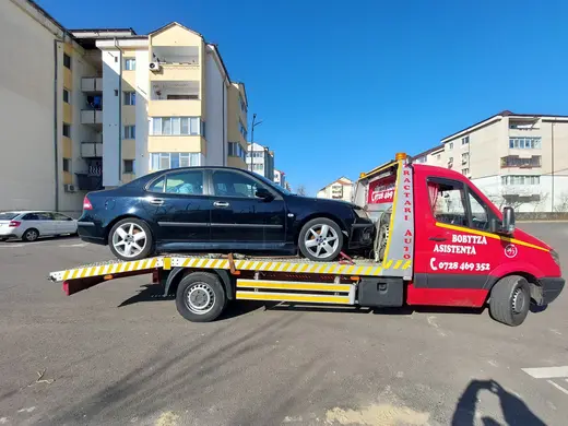 Sedan negru cu bara frontală avariată, încărcat pe platformă, în parcare la bloc