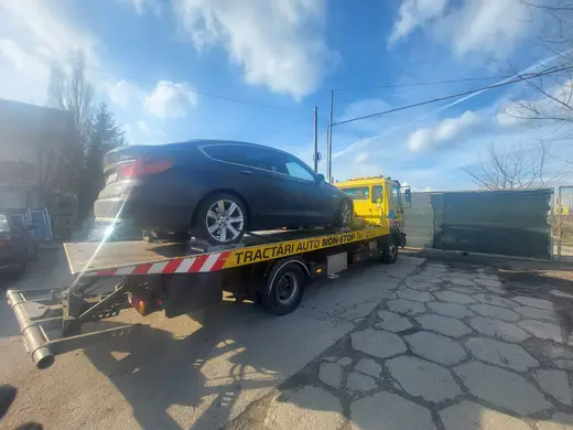 Sedan negru încărcat pe platforma hidraulică, tractat pe un teren viran