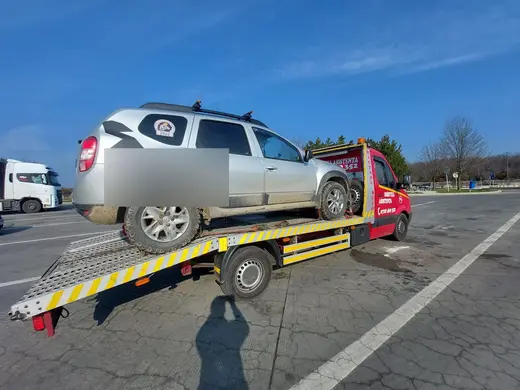 SUV argintiu încărcat pe platforma hidraulică, în parcare lângă camioane