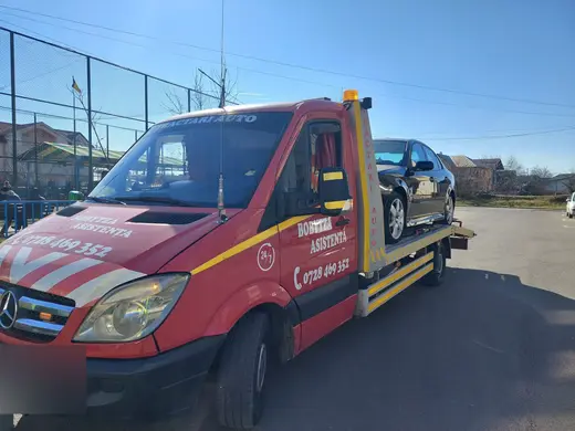 Sedan negru încărcat pe platforma hidraulică, ziua lângă un teren de sport