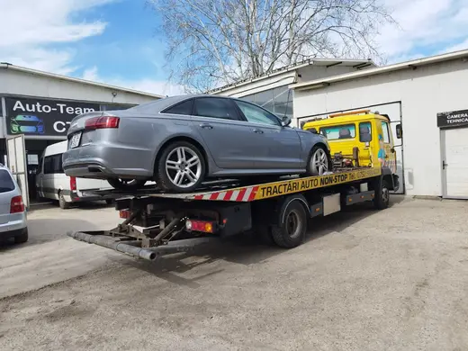 Sedan gri încărcat pe platforma hidraulică, în curtea unui service auto