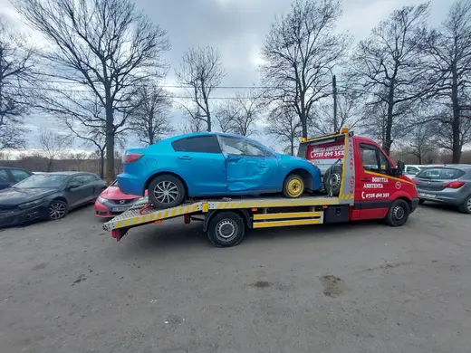 Hatchback albastru cu roata și aripa față avariate, încărcat pe platforma hidraulică