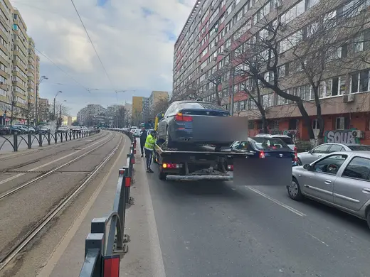 Sedan gri încărcat pe platforma hidraulică, tractat pe o stradă cu tramvai