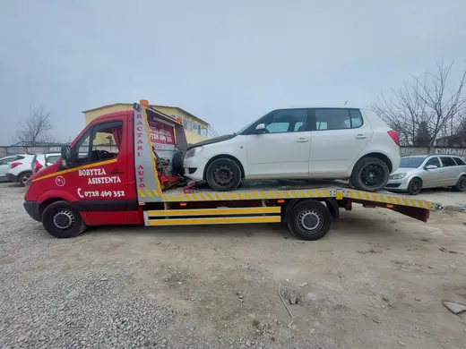Hatchback alb încărcat pe platforma hidraulică, pe teren viran lângă alte mașini