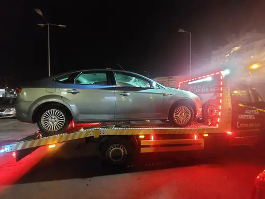 Autoturism gri-argintiu încărcat pe platformă hidraulică, tractare nocturnă cu semnalizare roșie