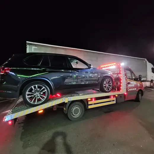SUV negru încărcat pe platformă hidraulică, tractare nocturnă într-o parcare