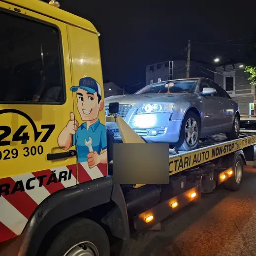 Autoturism argintiu tip berlină încărcat pe platformă, tractare nocturnă în oraș