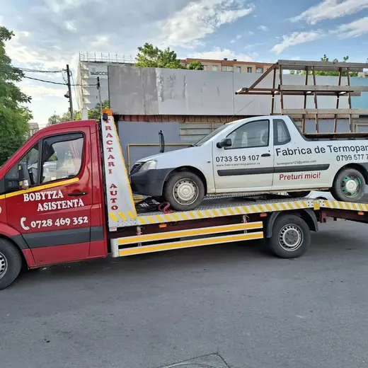 Autoturism alb încărcat pe platforma hidraulică a mașinii de tractare, în oraș