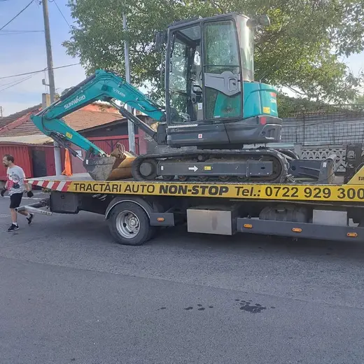 Miniexcavator încărcat pe platforma hidraulică, pe o stradă din cartier