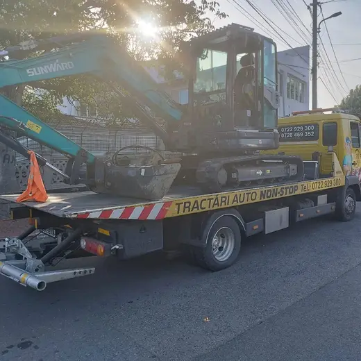 Miniexcavator cu braț articulat, încărcat pe platforma hidraulică de tractare