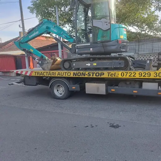 Miniexcavator încărcat pe platforma camionului de tractare, pe o alee