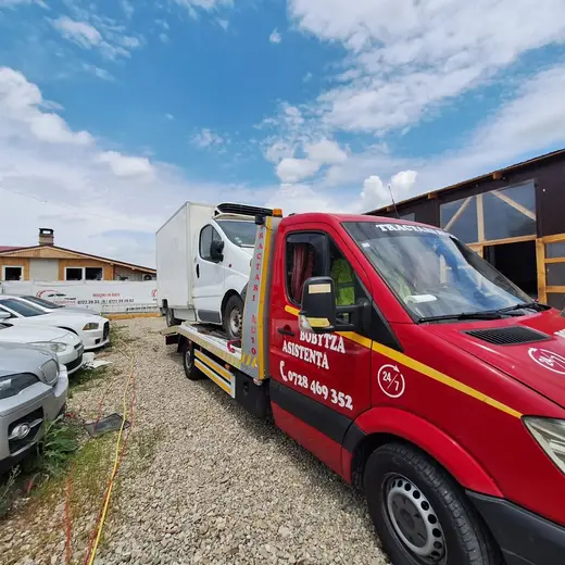 Duba albă cu cutie de marfă, încărcată pe platforma hidraulică, lângă un depozit auto