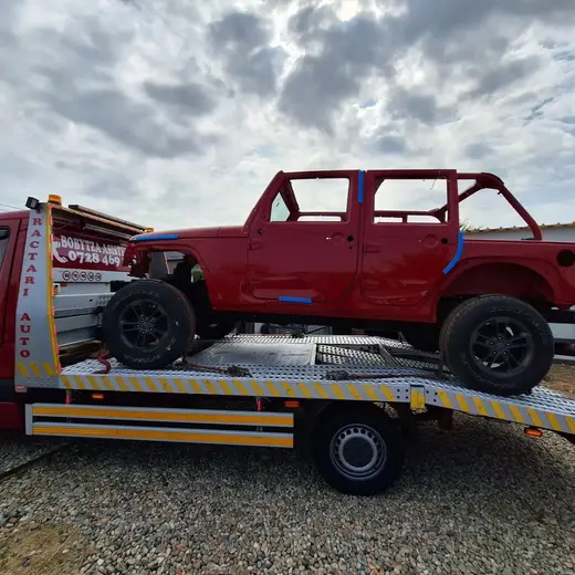 Vehicul roșu tip off-road, fără uși și geamuri, încărcat pe platformă hidraulică