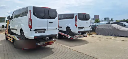 Două microbuze albe, fiecare încărcat pe propria platformă hidraulică, în parcare