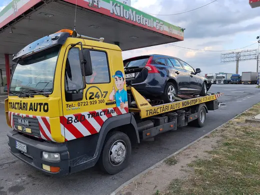 Autoturism break negru încărcat pe platforma hidraulică, lângă o benzinărie