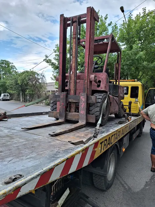 Stivuitor vechi, roșu, încărcat pe platforma camionului de tractare, pe stradă