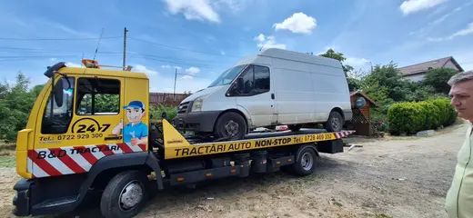 Autoutilitară albă încărcată pe platforma camionului de tractare, într-o curte