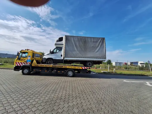 Camion cu prelată albă, încărcat pe platforma auto de tractare, ziua