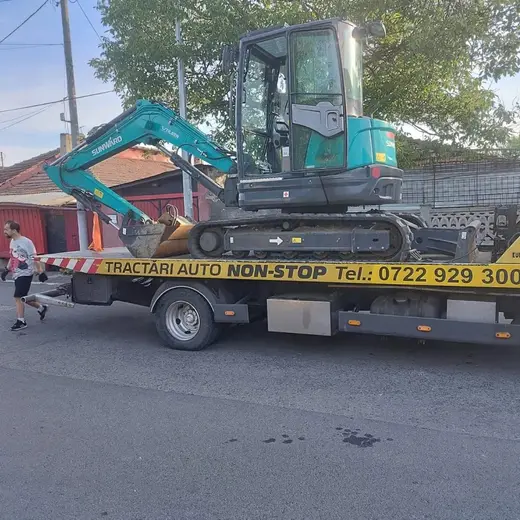 Miniexcavator verde, încărcat pe platforma camionului de tractare, pe stradă