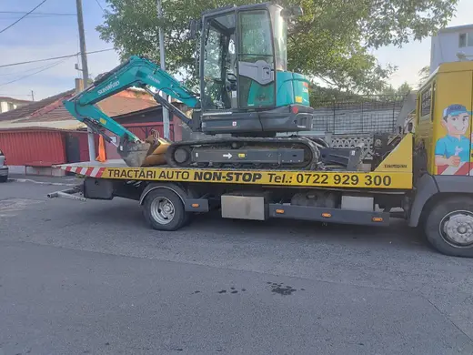 Miniexcavator verde pe șenile, transportat pe platforma hidraulică a camionului