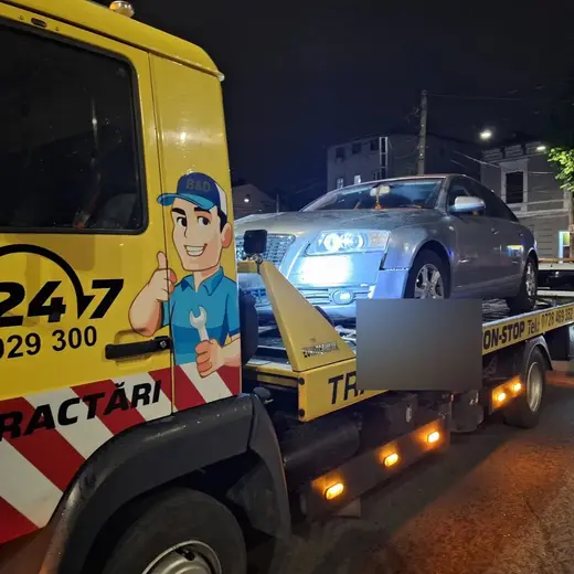 Autoturism argintiu încărcat pe platformă, intervenție de tractare pe timp de noapte