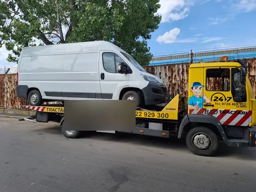 Autoutilitară albă încărcată pe platforma camionului galben de tractare, ziua