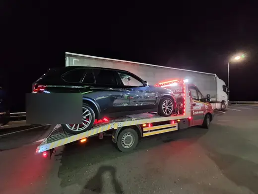 SUV negru încărcat pe platformă, tractare nocturnă lângă un camion cu remorcă