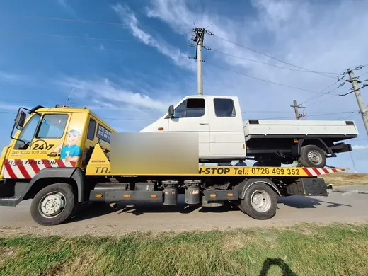 Camion basculantă alb, tractat pe platforma hidraulică, lângă un drum