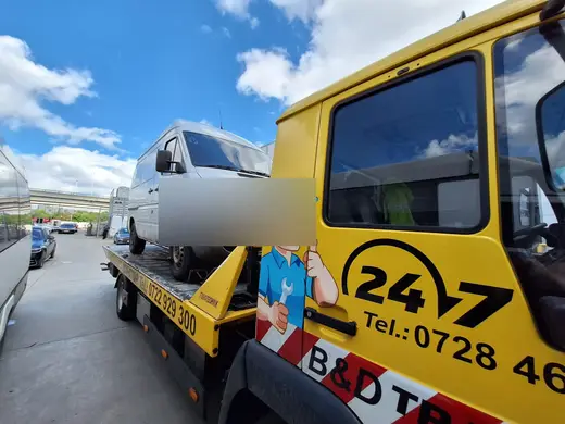 Camion cu ladă albă, încărcat pe platforma auto de tractare, în oraș