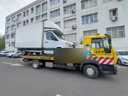 Autoutilitară cu ladă albă, încărcată pe platforma camionului de tractare