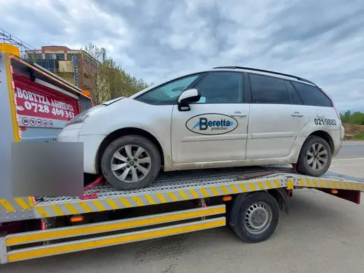 Autoturism alb tip monovolum, încărcat pe platforma hidraulică galbenă a camionului